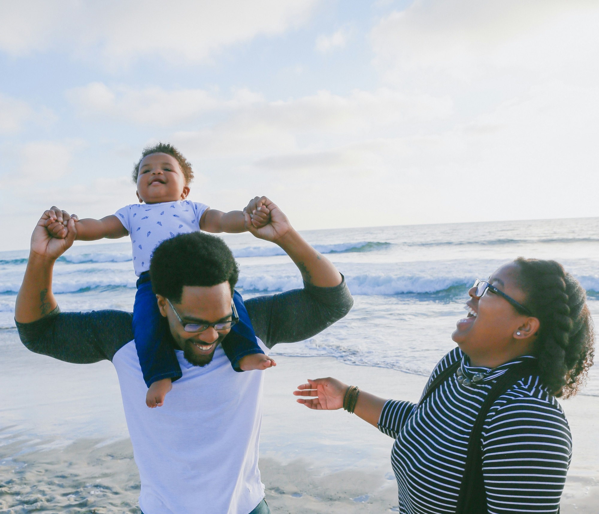 Happy Black family at the beach with baby sitting on father’s shoulders